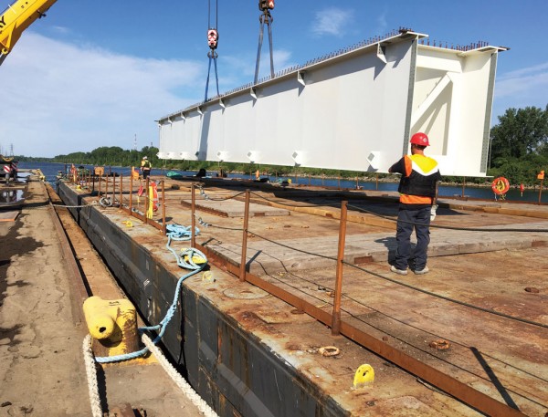 Castaloop stevedores load girders destined for massive new Champlain Bridge on St. Lawrence River under construction at Montreal.