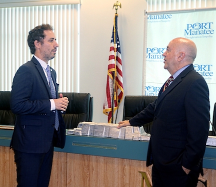 Martín de Antueno, deputy consul of Argentina, discusses trade opportunities with Port Manatee Executive Director Carlos Buqueras, who places his hand on a piece of aluminum imported into Port Manatee from Argentina.